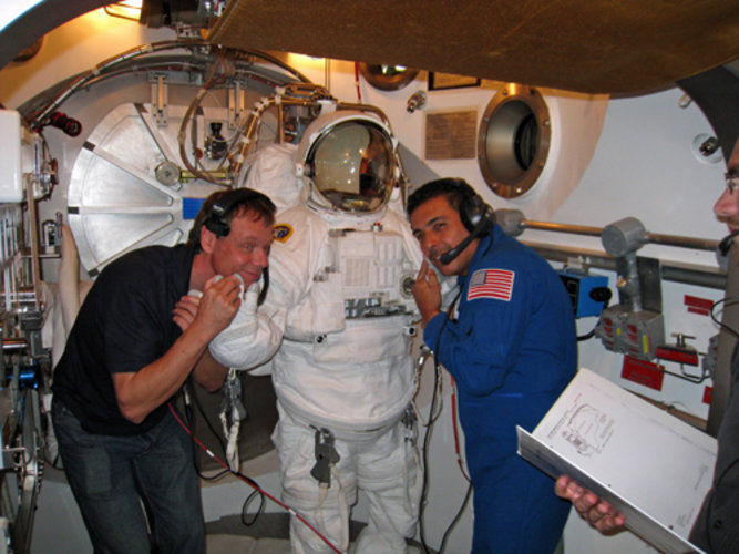 Det ser ut som om rymddräkten klappar oss på kinderna, men det vi gör är att känna om handskarnas elvärme fungerar.