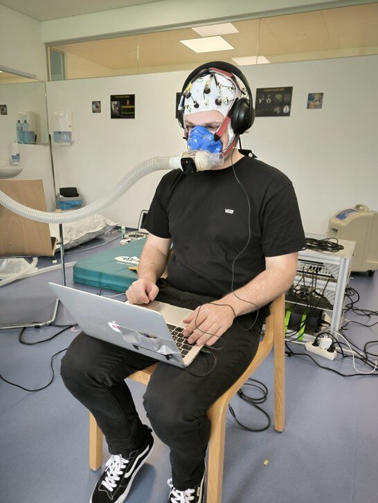 Neurocognitive experimental set-up during pilot testing. Participants will conduct a dual task containing both visual and auditory stimuli, whilst their brain activity is measured using an electroencephalogram (EEG)